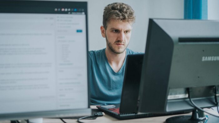 Muškarac pažljivo radi za računarom u kancelariji sa dva monitora