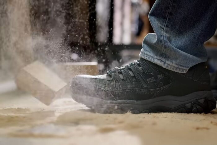 Crne radne cipele sa čeličnim vrhom na gradilištu dok cigla pada pored njih i podiže prašinu