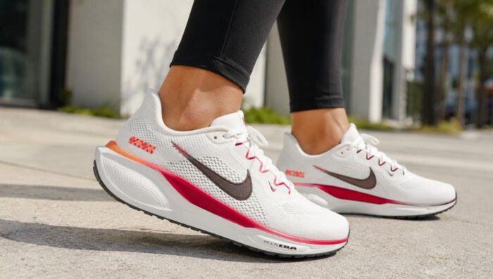 Žena u crnim helankama nosi bele Nike Air Zoom Pegasus 41 patike sa roze detaljima tokom šetnje gradskim pločnikom